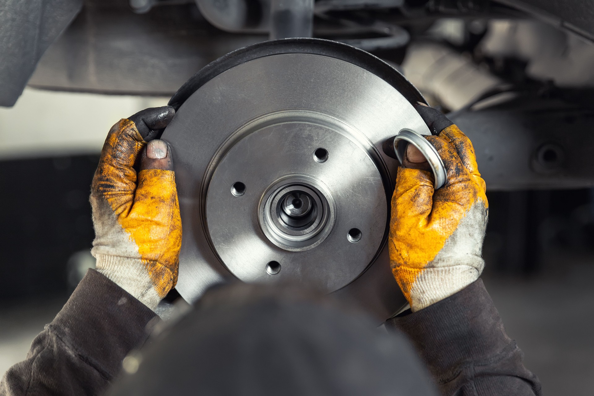 Closeup male tehnician mechanic greasy hands in gloves install new car oem brake steel rotor disk during service at automotive workshop auto center. Vehicle safety checkup and maintenance concpet