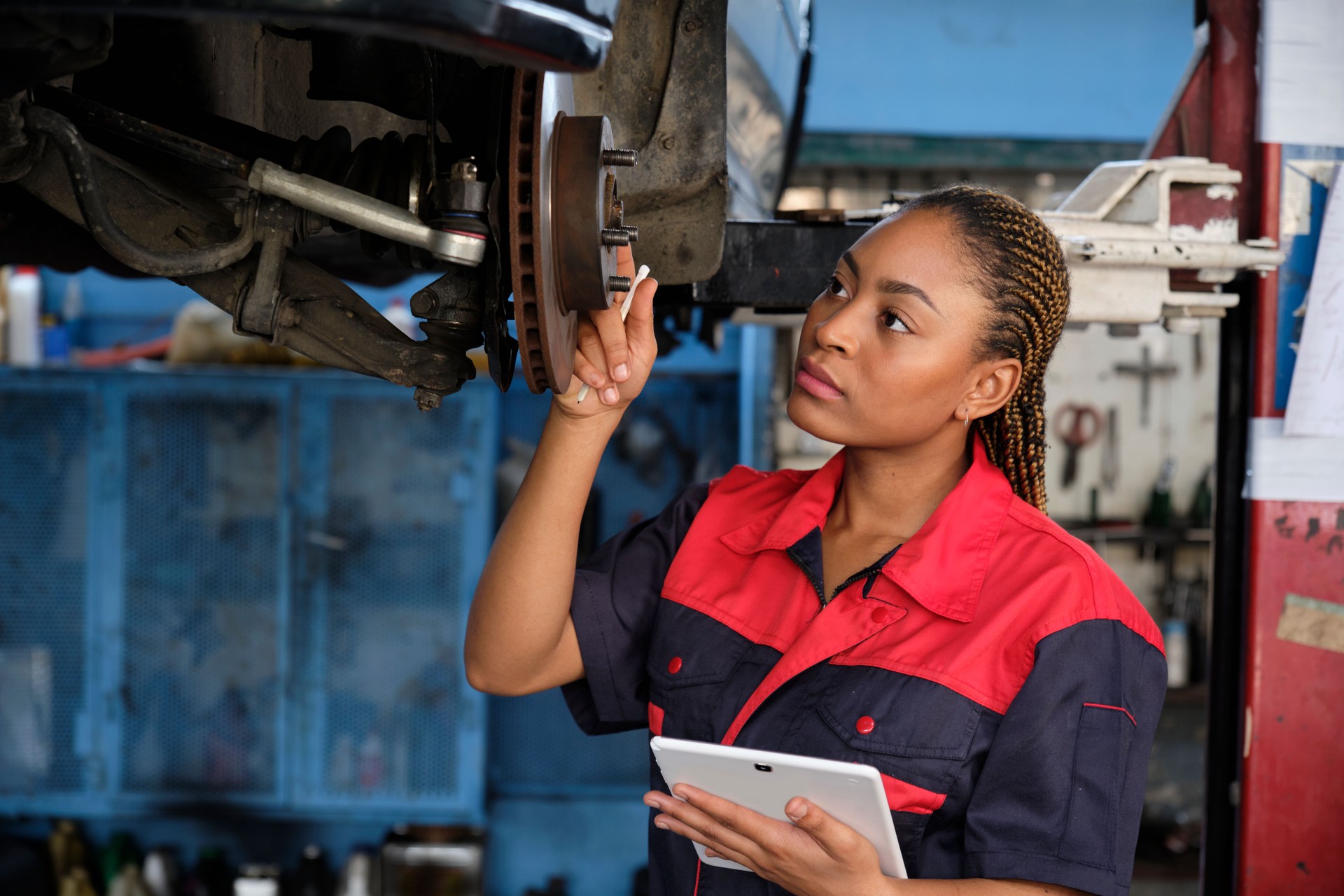 Black female mechanic checks car's brake disc and repairs checklist at garage.